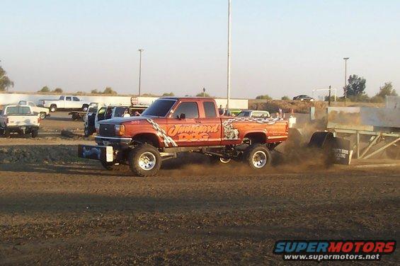 Orange lifted pickup truck with 'Junkyard Dog' graphics, side view, kicking up dust