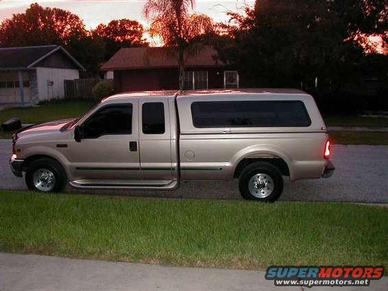 Side view of a 1999 Ford F-250 Super Duty pickup truck with a camper shell parked on a street
