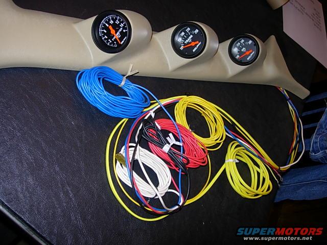 Tan gauge pod with three gauges and a bundle of colored wiring on a dark surface