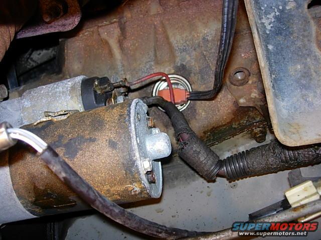 Starter motor with rusty casing and frayed wiring attached to a cast iron engine block