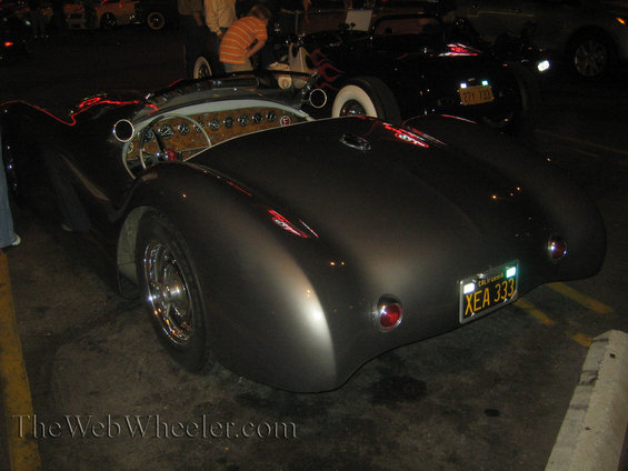 Rear view of a dark gray custom roadster with a California license plate XEA 333. Another car is visible behind it
