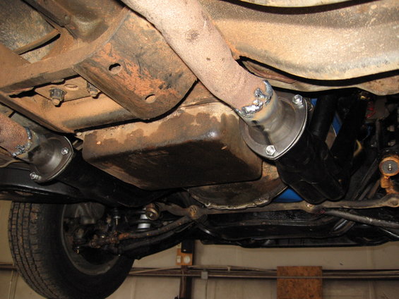 Underside view of a vehicle's exhaust pipes and frame, showing some rust and new welds on the pipes