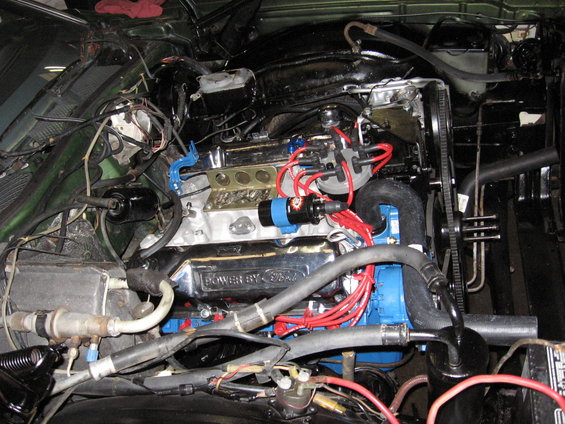 Close-up of a Ford V8 engine bay with blue painted block and chrome valve covers reading "POWER BY Ford"