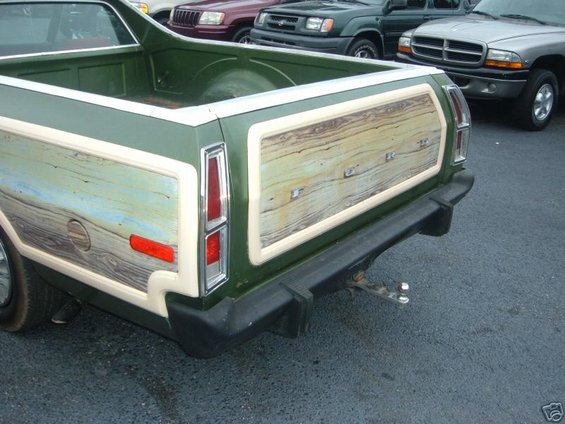 Rear of green Ford Ranchero with wood grain paneling on tailgate. Other vehicles visible behind it