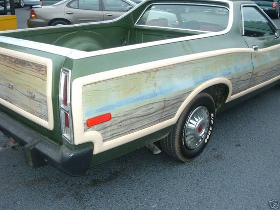 Green pickup truck with wood paneling, rear quarter view, showing a red taillight and chrome hubcap