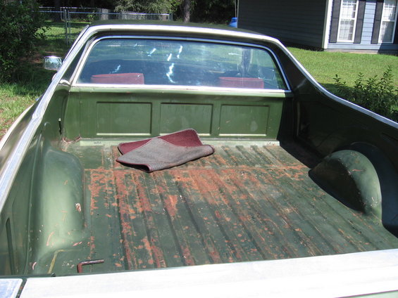 Back of a green Ford Ranchero pickup truck bed with a rug on the floor. The bed is worn and rusty