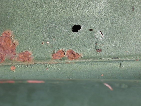 Close-up of green metal with rust spots and a hole