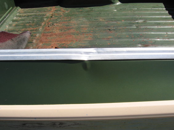 Green truck bed with rust and a dented metal trim piece
