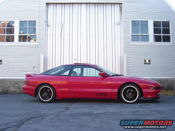 Red coupe with black roof and gold-trimmed wheels, side view