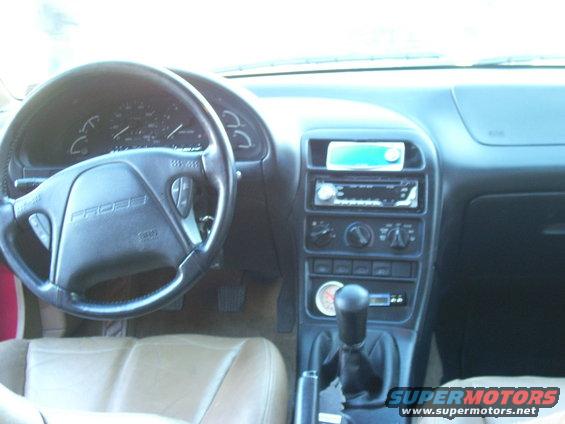 Interior shot of a car, showing the steering wheel with 'PROBE' text, dashboard, center console with radio and gear shifter, and tan leather seats