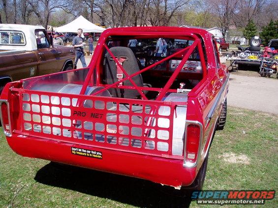 Red pickup truck with roll cage and racing seat, rear view. Modified bed with Pro Net