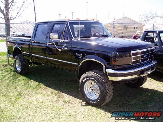 Black Ford F-250 pickup truck, four-door cab, lifted suspension, chrome wheels, parked on grass