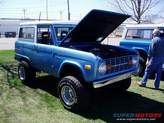 Blue 1973 Ford Bronco with hood open, parked next to another Bronco