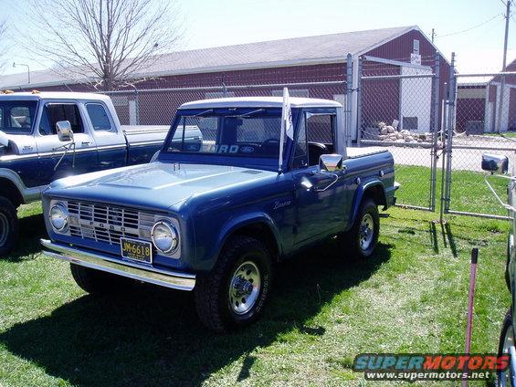 Blue Ford Bronco parked on grass next to a blue and white pickup truck