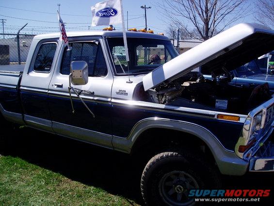 Two-tone Ford pickup truck, hood open, with Ford flags on roof