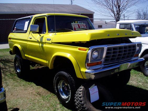 Yellow 1978 Ford Bronco with hood open, "FOR SALE" sign in window, parked on grass next to another white vehicle