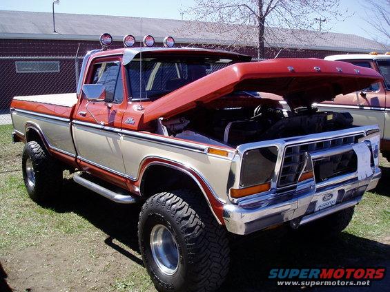 Two-tone red and tan Ford F-Series pickup truck with hood open, lifted suspension, and aftermarket lights