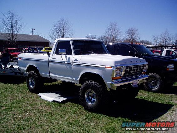 White Ford pickup truck with lifted suspension and chrome grille, parked on grass
