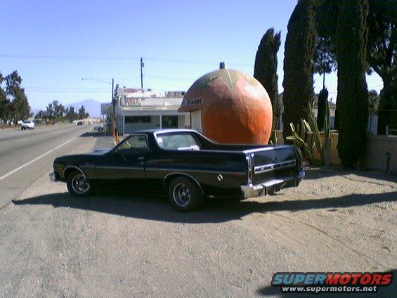 black 1973 Ford Ranchero parked by a giant orange roadside attraction