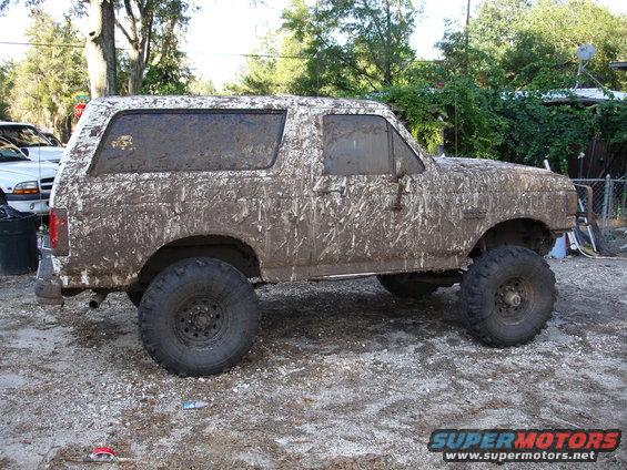 Mud-covered 1989 Ford Bronco parked on gravel. Lifted suspension and large tires visible