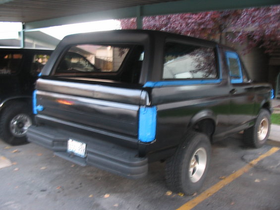 1991 Ford Bronco parked under a carport, rear view. Blue tape is visible on the body panels