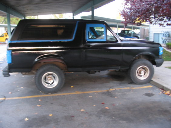 Side view of a black 1991 Ford Bronco parked under a covered area. Blue tape is on the windows and rear bumper