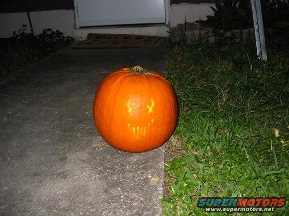 Carved pumpkin with a face on a concrete path next to grass