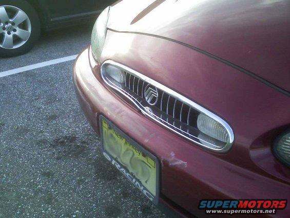 Red 1998 Mercury Sable front end with grille and headlight visible; another car's wheel is in the background