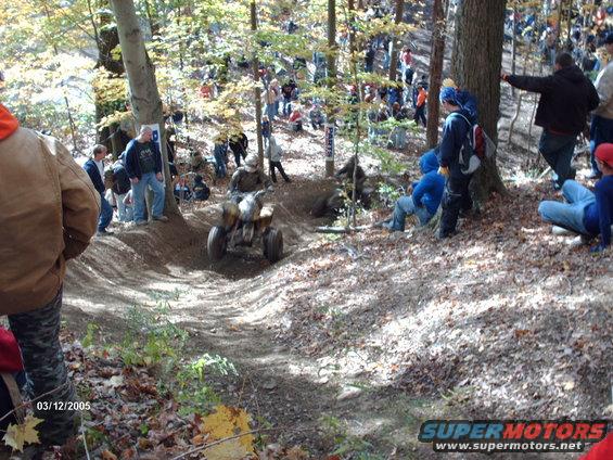 ATV navigating a wooded trail with spectators watching from the sides
