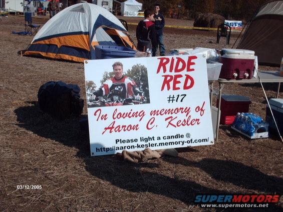 Memorial sign with a photo of a man on a motorcycle, text reads 'RIDE RED #17 In loving memory of Aaron C. Kesler'