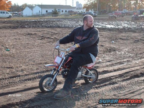 Man riding a small red and white dirt bike on a muddy track