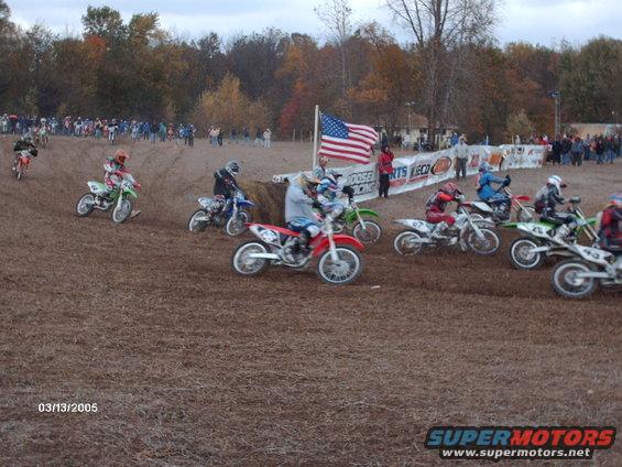 Dirt bikes racing on a track with spectators in the background and an American flag