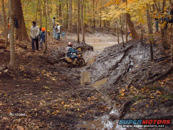 Motorcycle rider navigating a muddy trail in a forest during autumn