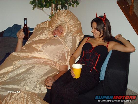 Guy in a tan inflatable costume holding a beer, and a woman in a devil costume holding a cup, sitting on a couch