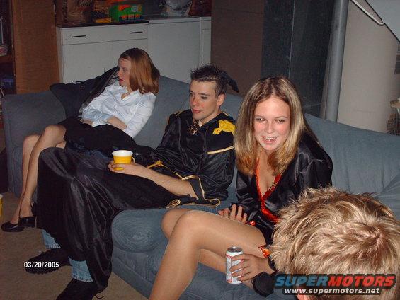 People in costumes sit on a couch. One person holds a yellow cup, another holds a soda can