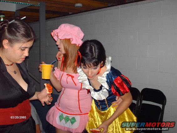 Three women in costumes, one in black, one in pink, and one as Snow White, holding food and drinks