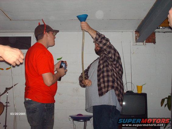 Two men in a basement, one holding a funnel and tube, the other watching. Date stamp 03/20/2005