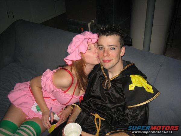 Woman in pink costume kisses man in black and gold costume on a couch