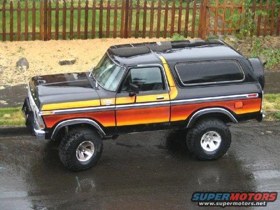 1978-1979 Ford Bronco with orange and yellow stripe graphics, parked on wet asphalt