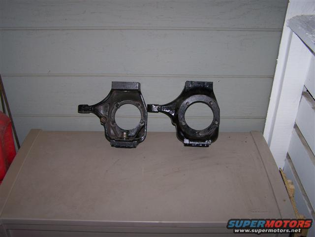 Pair of black metal steering knuckles on a tan surface