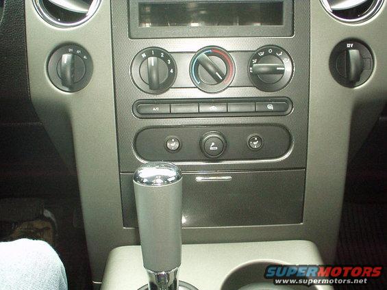 Gray dashboard interior with chrome-topped gear shifter, climate controls, and a 12V power outlet