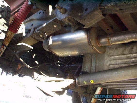 Underside view of a vehicle's exhaust muffler, driveshaft, leaf springs, and red shock absorber