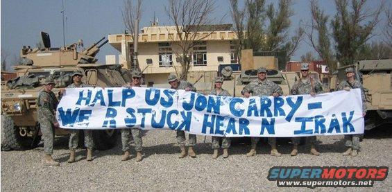 Soldiers in front of military vehicles hold a banner that says 'HALP US JON CARRY - WE R STUCK HEAR N IRAK'