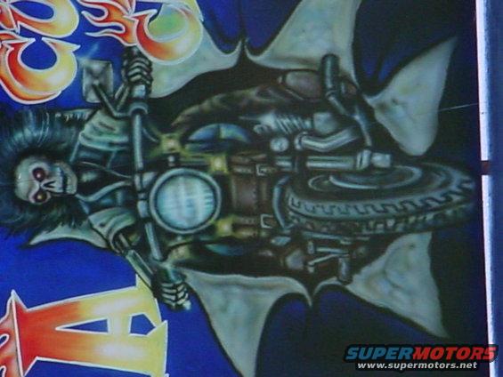 Airbrushed artwork of a skeleton on a motorcycle with flames and wings, on a blue background. Supermotors.net logo in lower right
