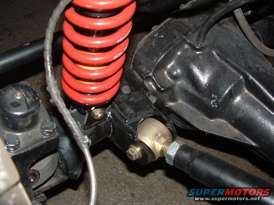 Close-up of red coil spring and black suspension parts with a "SUPERMOTORS.NET" watermark