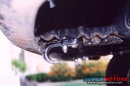 Close-up of a metal tow hook attached to a vehicle's frame, with a small metal tag visible