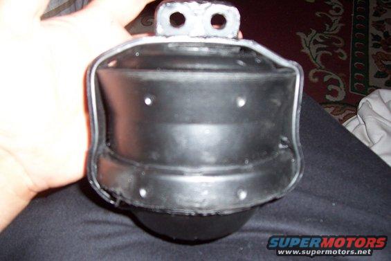Hand holding a black engine mount with metal brackets