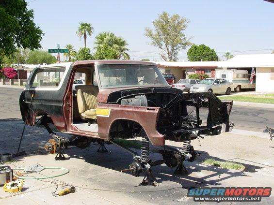 Brown and white Ford Bronco body on jack stands, front end removed, interior visible