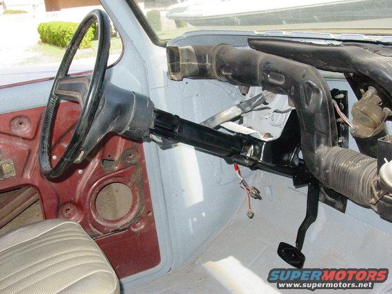 Interior view of a vehicle's dashboard and steering wheel, showing exposed metal and wiring