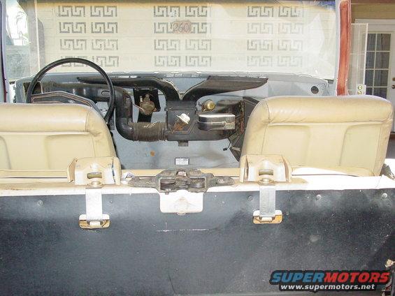 Interior view of a vehicle with tan seats, dashboard, and steering wheel removed. The rear panel has latches